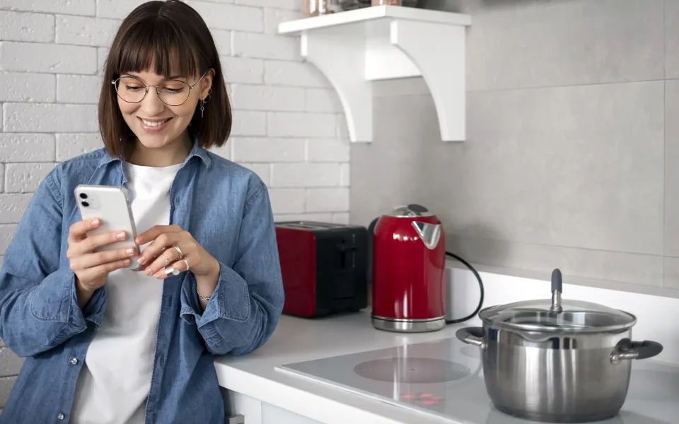 Mulher a usar o telemóvel na cozinha