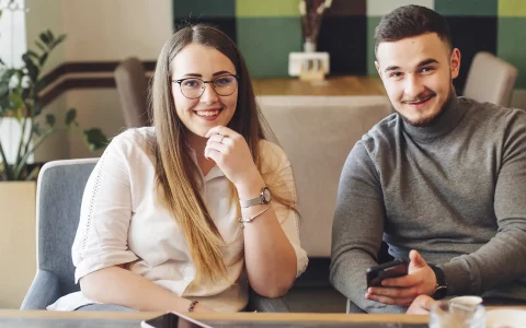 Casal sentado no sofá enquanto sorri com o telemóvel na mão