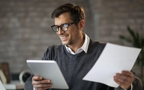 Homem a sorrir com o tablet e papéis na mão