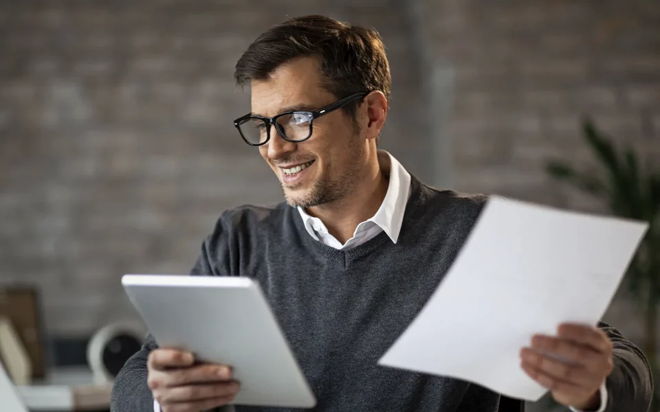 Homem a sorrir com o tablet e papéis na mão