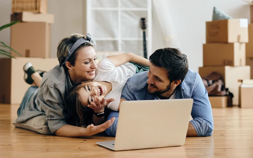 Família a sorrir no chão da sala a olhar para o computador portáril