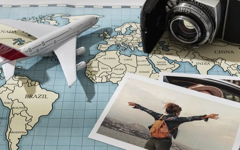 Composição temática de viagens com um avião em miniatura, uma câmara fotográfica antiga e fotografias de paisagens pousados sobre um mapa-mundo.