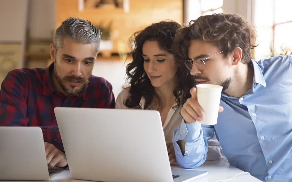 Três colegas de trabalho reunidos à volta de um computador portátil a analisar o ecrã com atenção