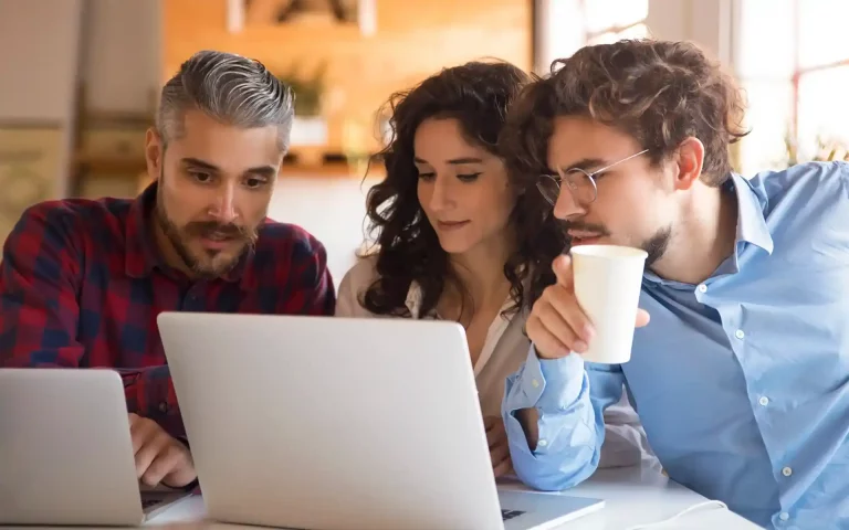 Três colegas de trabalho reunidos à volta de um computador portátil a analisar o ecrã com atenção