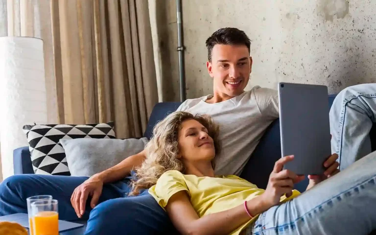 Jovem casal relaxado no sofá a usar um tablet juntos no interior de uma sala de estar moderna.