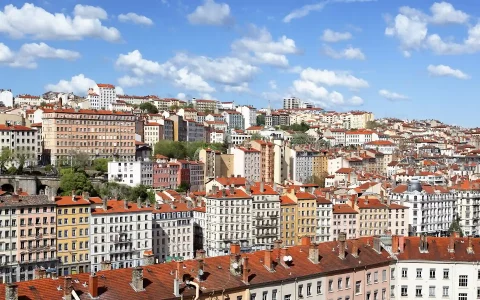 sliderarrendamento ezgif.com jpg to webp converter Vista panorâmica de vários edifícios residenciais com telhados vermelhos numa colina sob um céu azul com nuvens.